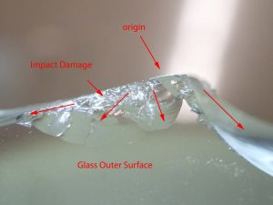Figure #3: Photo micrograph of the preserved portion of the failure origin. Although the entire failure origin was not preserved, the remaining part shows severe impact to the glass. (Mag. 15X).